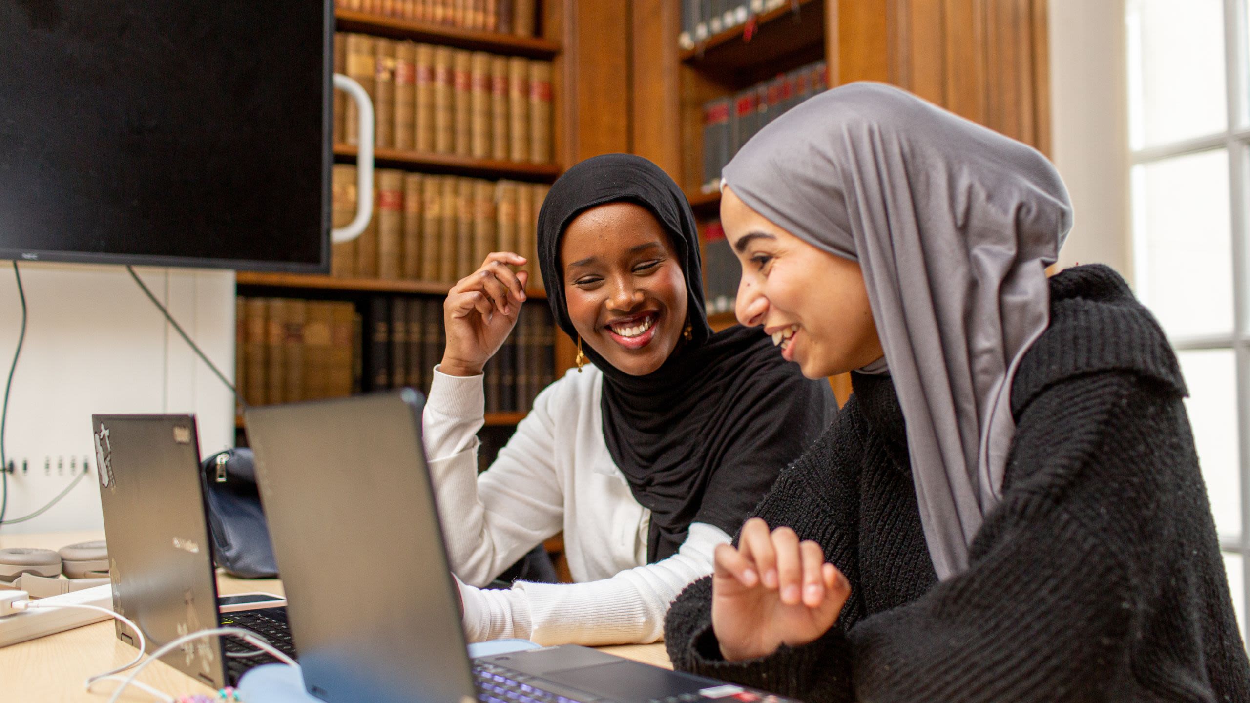 Two students smiling while looking at a laptop in Main Library