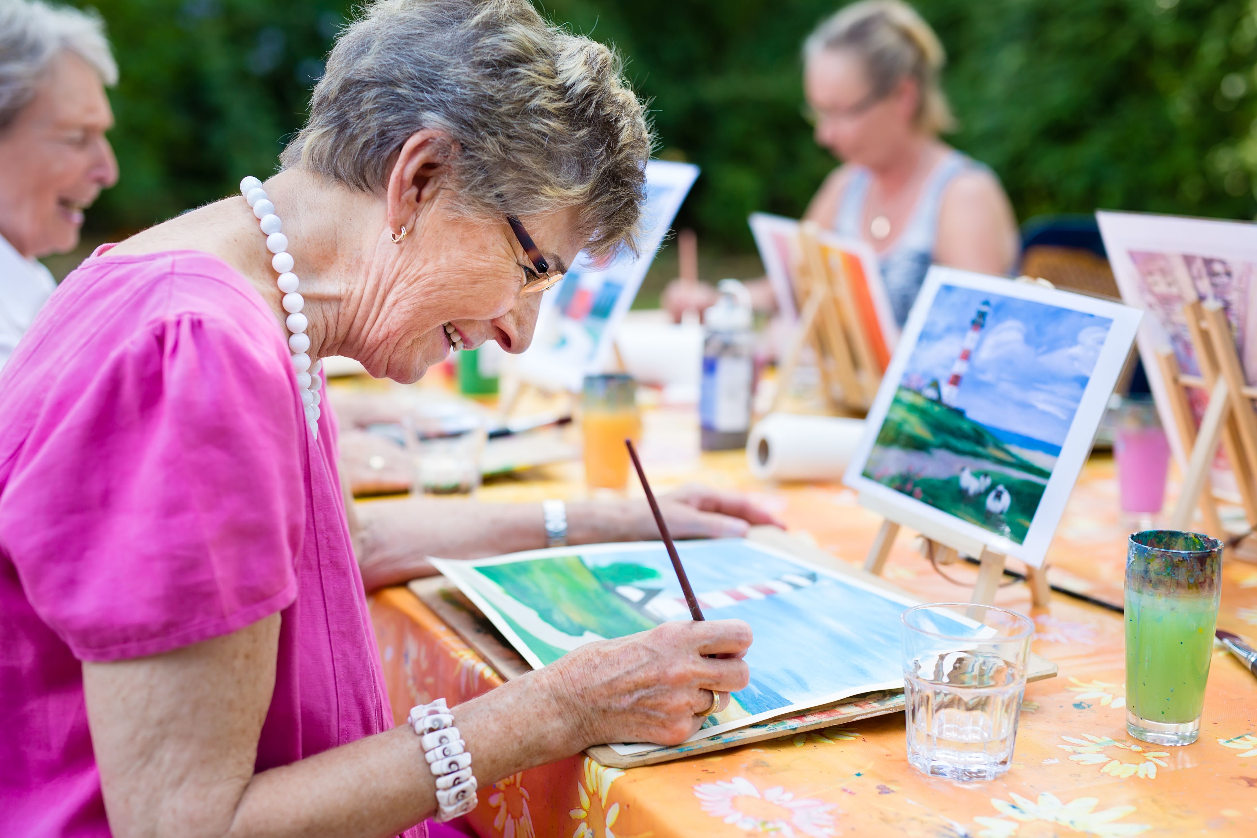 An older woman painting outside in a group of other women